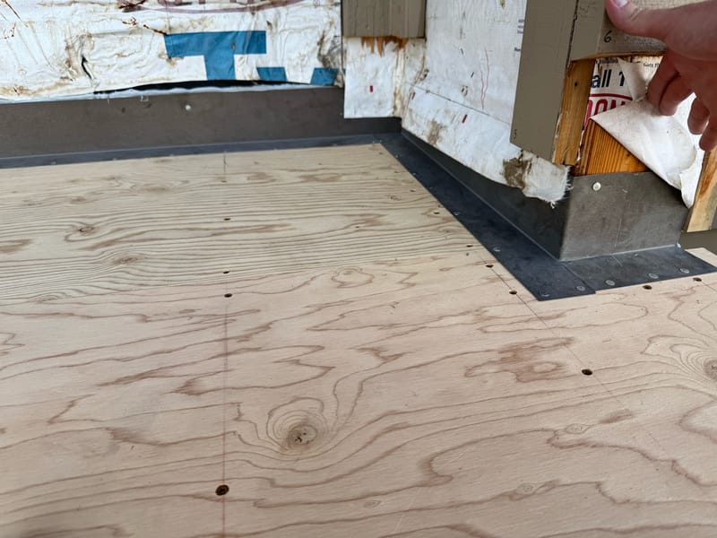 Metal pan flashing formed at a deck post base and tucked behind the weather-resistive barrier.
